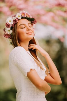 Portrait of young woman with wreath of fresh flowers on head in the park
