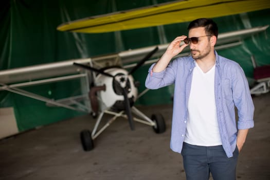 Young handsome young pilot checking airplane in the hangar and using mobile phone