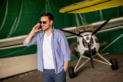 Handsome young man using mobile phone in the airplane hangar