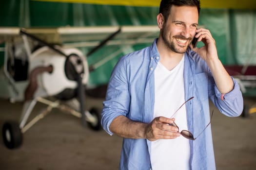 Handsome young man using mobile phone in the airplane hangar