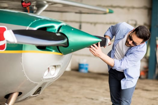 Handsome young pilot checking airplane  in the hangar