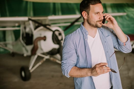 Handsome young man using mobile phone in the airplane hangar