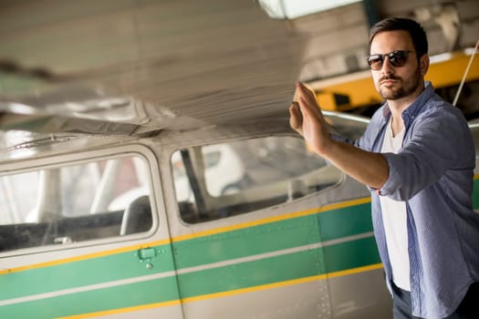 Handsome young pilot checking his ultralight airplane in the hangar before flight