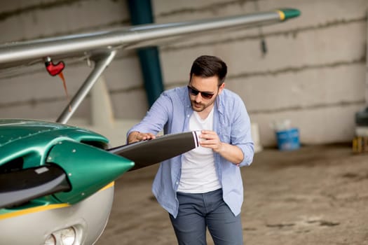 Handsome young pilot checking his ultralight airplane in the hangar before flight