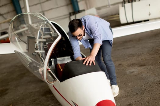 Handsome young pilot checking his ultralight airplane in the hangar before flight