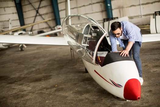 Handsome young pilot checking his ultralight airplane in the hangar before flight