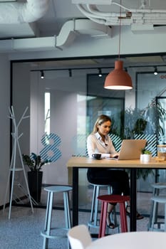 A professional woman with long hair sits at a modern desk in her office, focused on her computer screen while working on a project.