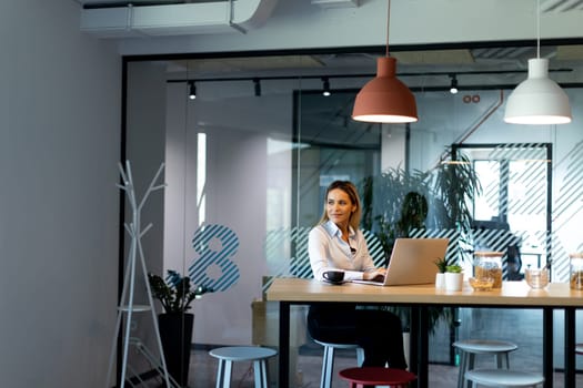 A professional woman with long hair sits at a modern desk in her office, focused on her computer screen while working on a project.