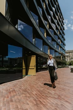 A woman in business attire walks along a brick path outside a sleek, architectural office building under a clear blue sky.