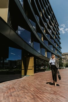 A woman in business attire walks along a brick path outside a sleek, architectural office building under a clear blue sky.