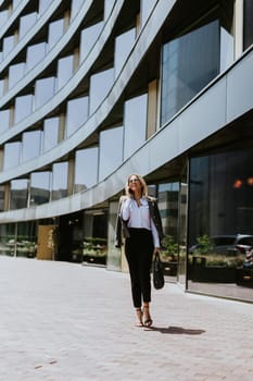 A woman in business attire walks along a brick path outside a sleek, architectural office building under a clear blue sky.