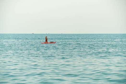 A person stands on a paddleboard, navigating through tranquil sea waters. The sky is overcast, creating a peaceful atmosphere as they enjoy a leisurely outing on the water.