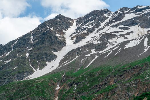 A majestic mountain rises with patches of snow and vibrant green slopes under a clear blue sky. The beauty of nature is highlighted in this serene alpine setting.