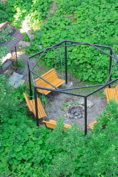 A peaceful seating arrangement made of wooden benches encircles a fire pit. The area is nestled in vibrant green foliage, creating a serene outdoor retreat perfect for gatherings.