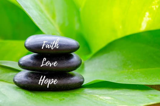 Faith, love and hope text on black zen stones. Faith and love concept.