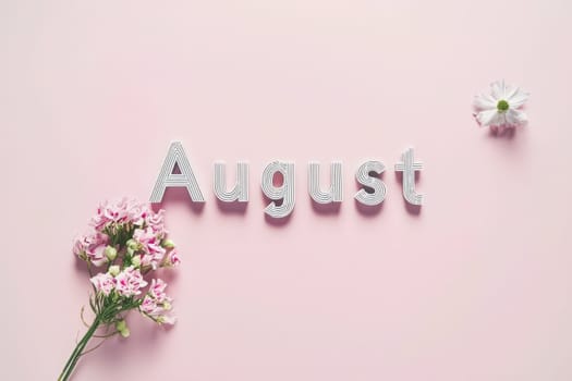 The word August is artistically arranged in striped letters on a smooth pastel pink surface, accompanied by pink flowers and a single white bloom, creating a vibrant yet soft aesthetic.