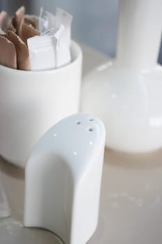 A white salt shaker sits beside sugar packets in a modern setting.