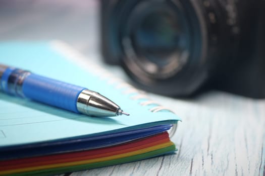 A colorful notebook and pen are placed near a camera on a desk.