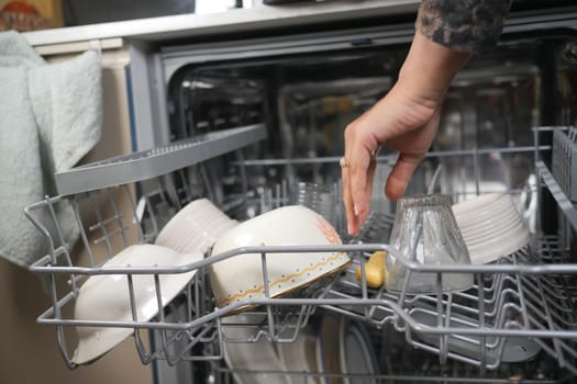A person is carefully arranging clean bowls and glasses in a dishwasher.