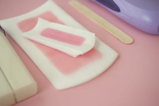 Various waxing supplies laid out neatly on a soft pink surface.