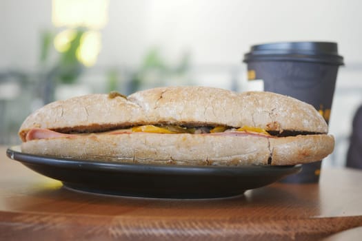A tasty sandwich on a plate next to a cup of coffee in a quiet cafe.