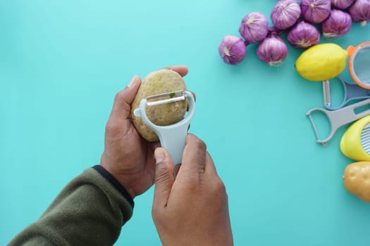A hand peels a potato while surrounded by fresh ingredients.