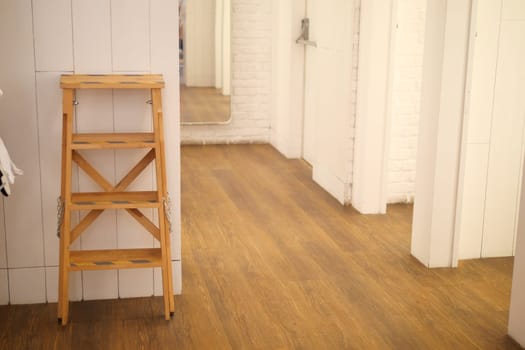 Wooden ladder positioned in a bright, minimalistic hallway with white walls.
