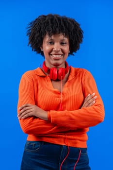 Smiling African American woman wearing red headphones, posing confidently with arms crossed against a blue background. Modern fashion, casual style, technology, self-assurance, and positivity.vertical