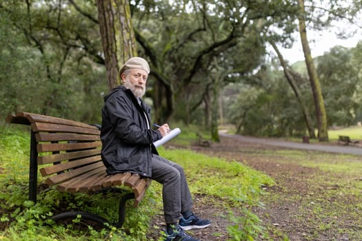 Elderly man writing notes while sitting on bench in a tranquil park