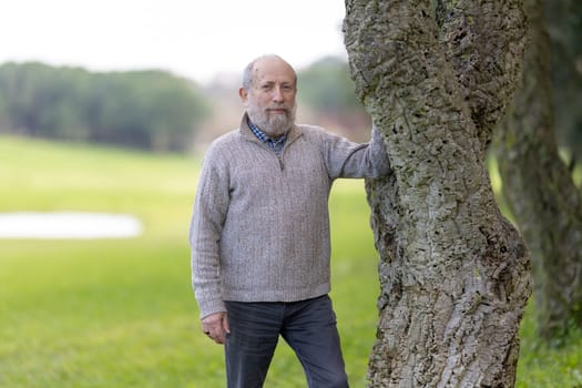 Confident senior golfer resting against a cork oak tree, enjoying the serene atmosphere of a golf course