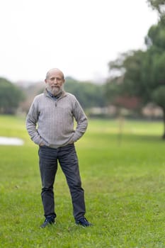 Portrait of a content senior man standing in a green park, enjoying his retirement