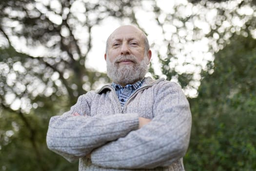 Portrait of a confident senior man standing with arms crossed in a park, enjoying the fresh air and tranquility of nature