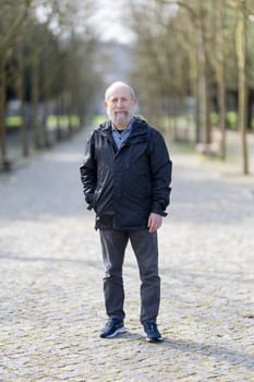 Portrait of a confident senior man standing on a paved path in a park, enjoying the fresh air and tranquility of nature
