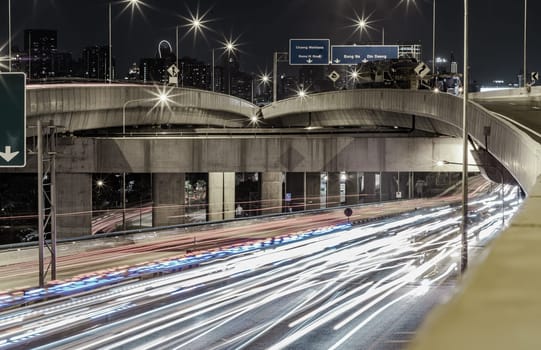 Bangkok, Thailand - Jan 10, 2025 - A nightscape view with bright glowing light trails effect of many cars headlights and rear lights on urban expressway of Bangkok. Long exposure for Light curve lines, use it as wallpaper, Poster and Copy space, Selective focus.