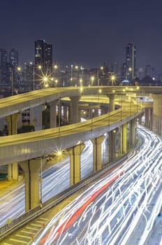 Bangkok, Thailand - Jan 10, 2025 - A nightscape view with bright glowing light trails effect of many cars headlights and rear lights on urban expressway of Bangkok with Skyscrapers in the background. Long exposure for Light curve lines, use it as wallpaper, Poster and Space for text, Selective focus.