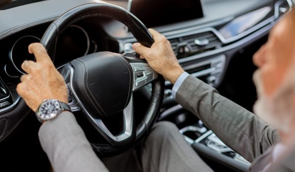 Cheerful elderly man in a suit driving leisurely, basking in the warm glow of a bright day