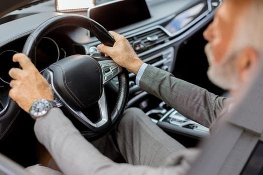 Cheerful elderly man in a suit driving leisurely, basking in the warm glow of a bright day