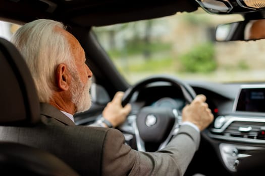 Cheerful elderly man in a suit driving leisurely, basking in the warm glow of a bright day