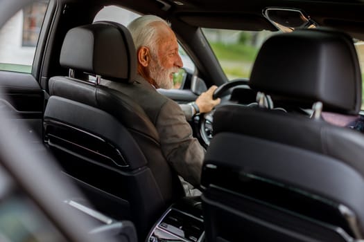 An elderly gentleman, dressed in a suit, confidently drives a modern car through a bustling city street on a bright, sunny day