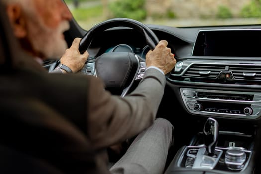 Cheerful elderly man in a suit driving leisurely, basking in the warm glow of a bright day