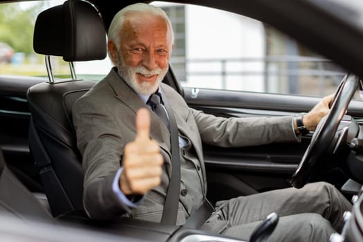 An elderly man in a suit smiles with approval from the drivers seat