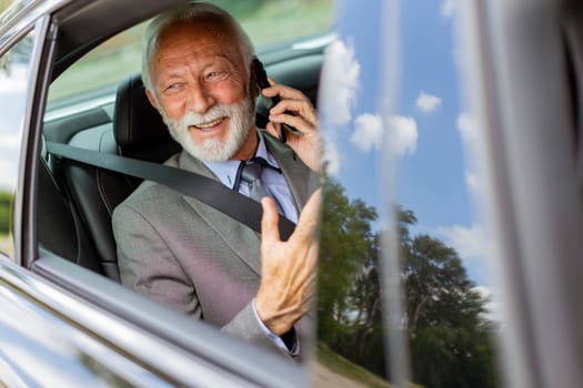 Suave senior man converses on his cell during a leisurely car ride, exuding charm and confidence