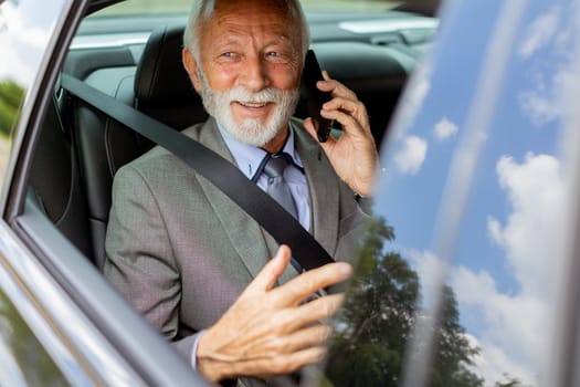 Suave senior man converses on his cell during a leisurely car ride, exuding charm and confidence