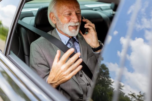 Suave senior man converses on his cell during a leisurely car ride, exuding charm and confidence