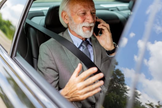 Suave senior man converses on his cell during a leisurely car ride, exuding charm and confidence