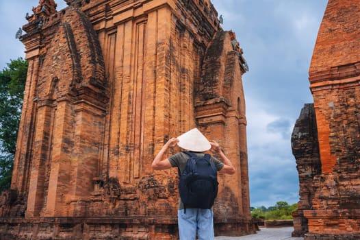 back of Asian male tourist traveler in Vietnamese cone hat Non La on Cham Towers of Po Nagar in Nha Trang in Vietnam in Asia