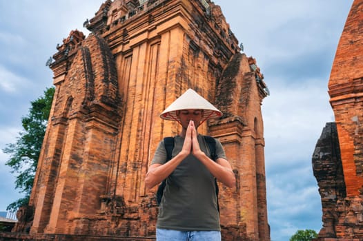 man in a Vietnamese cone hat non la prays at the ancient Po Nagar Cham Towers in Nha Trang, Vietnam. The concept of travel in Asia