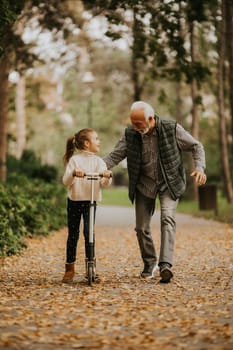 Senior man teaching his granddaughter how to ride kick scooter in the autumn park