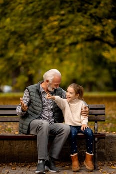 Handsome grandfather spending time with his granddaughter on bench in park on autumn day