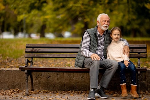 Handsome grandfather spending time with his granddaughter on bench in park on autumn day